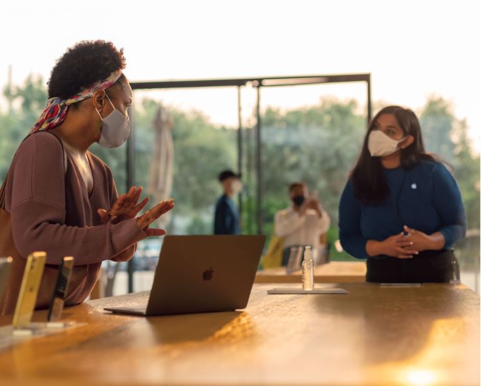 Cliente hablando con un representante de Genius Bar mientras está delante de iPhones y un ordenador.