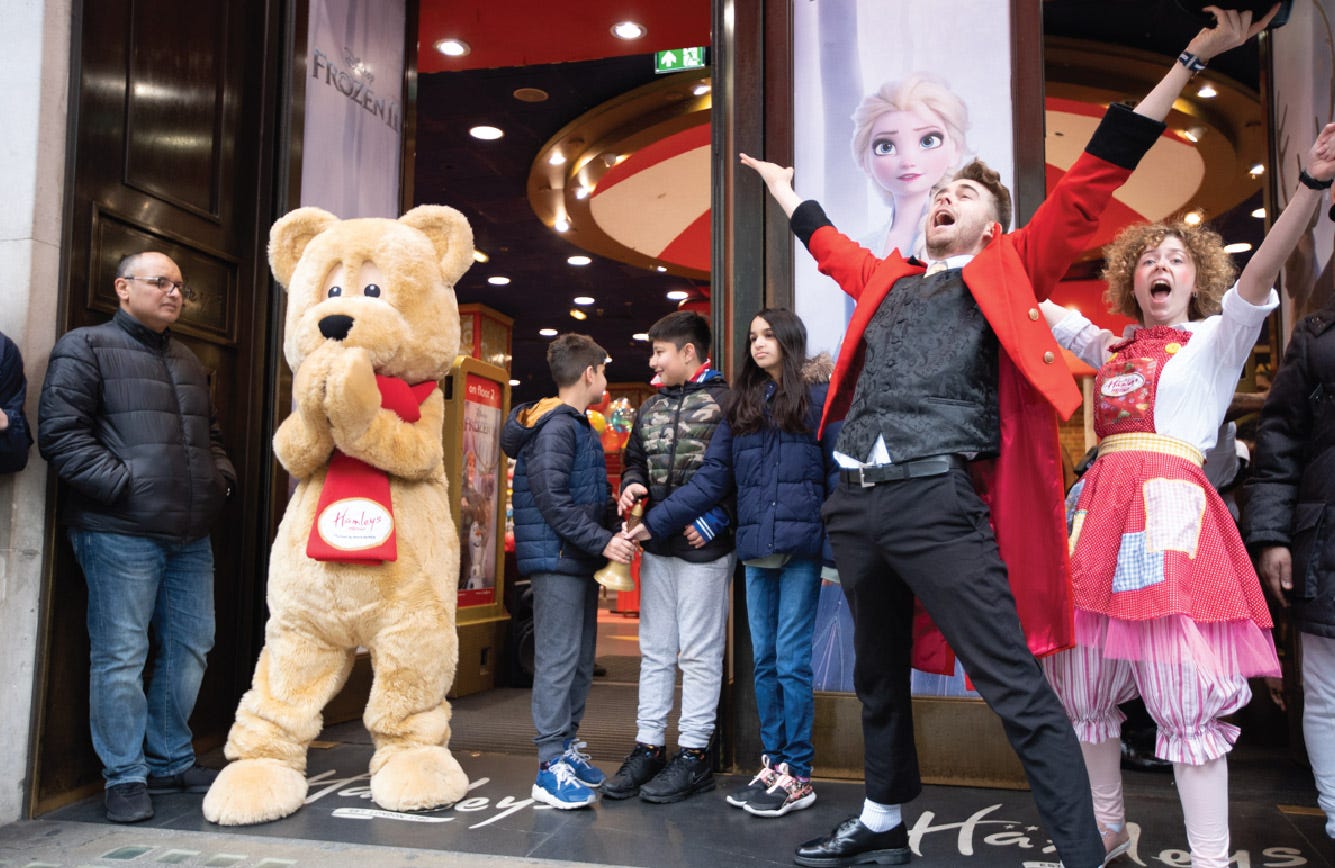 Bear mascot, shoppers, and event singers outside a Hamleys store 