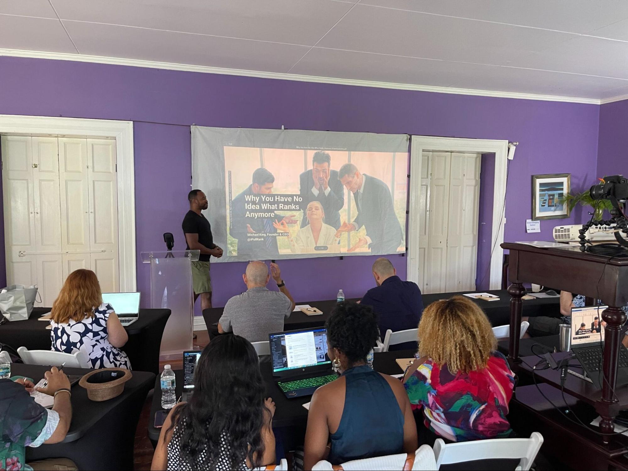 A speaker presenting in front of a small crowd at a BarbadosSEO conference