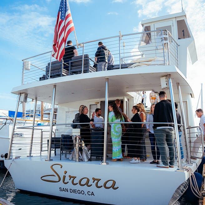 A multi-level yacht named "Sirara" from "San Diego, CA" with guests on board, some on the upper deck with an American flag.